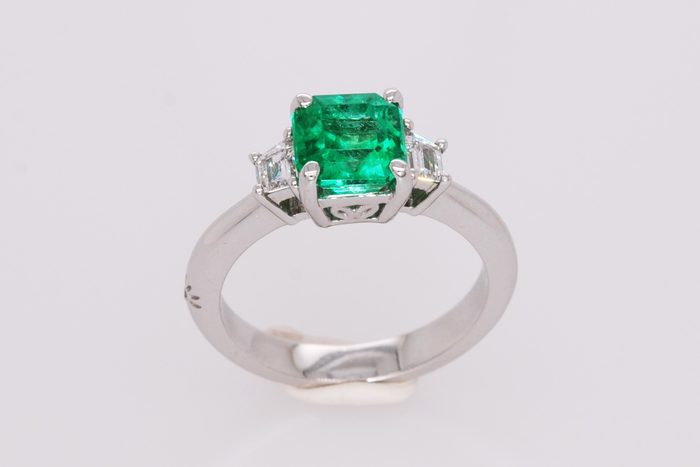 Emerald-cut green gemstone ring with two side diamonds on a white gold band