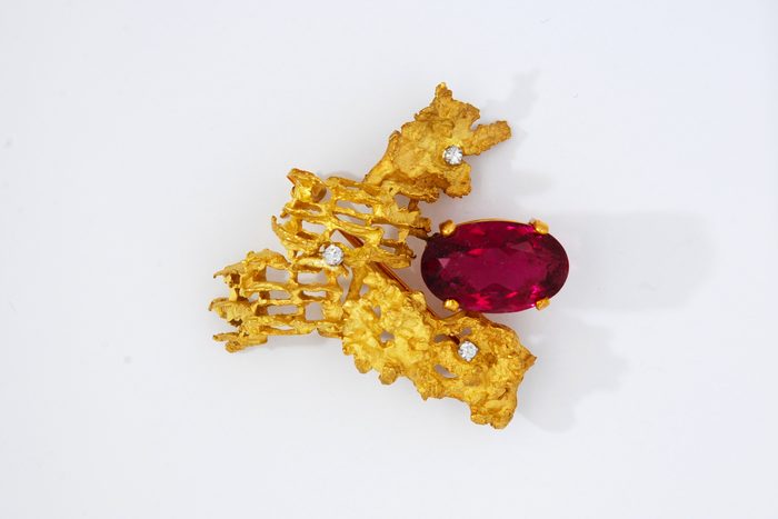 Textured gold brooch set with a red oval gemstone and small diamonds
