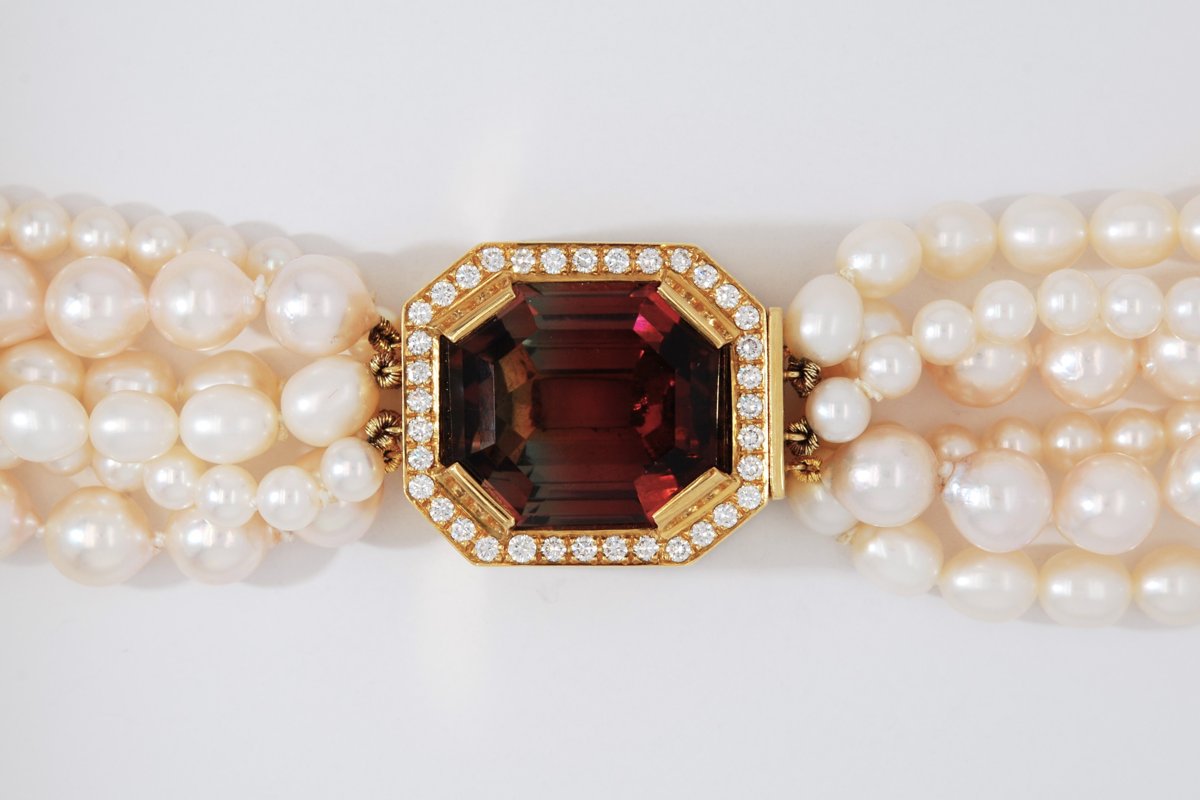 Multi-strand pearl necklace with a gold clasp set with a large gemstone and a diamond border